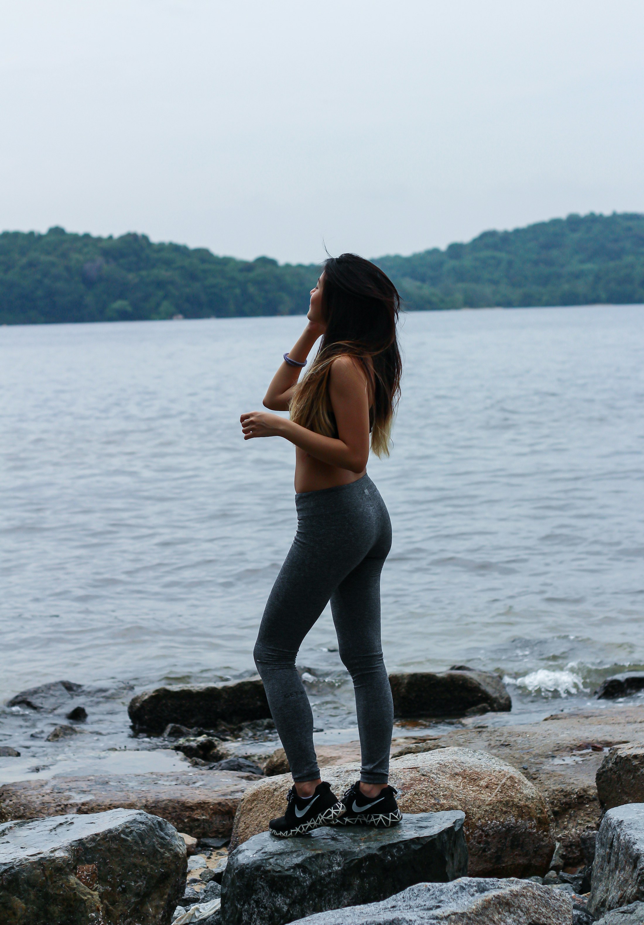 A woman standing on rocks beside a lake, looking out across the water