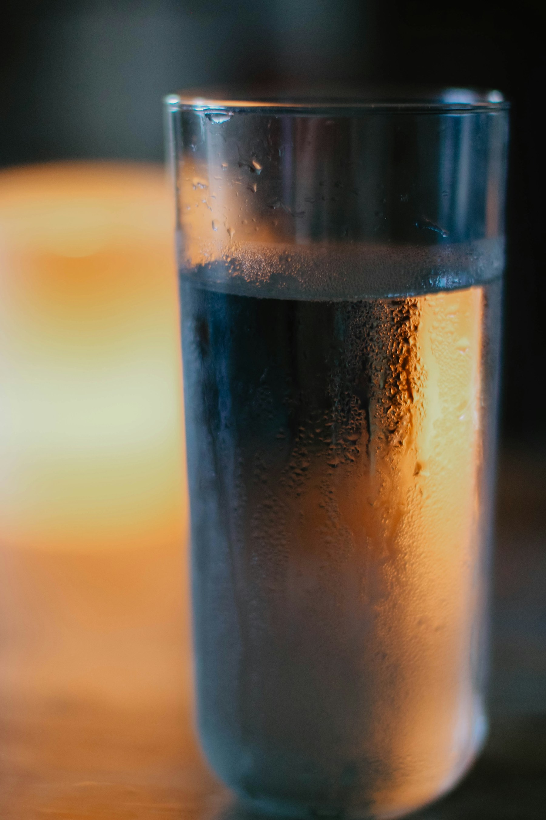 A tall glass of water with condensation, lit warmly from the side